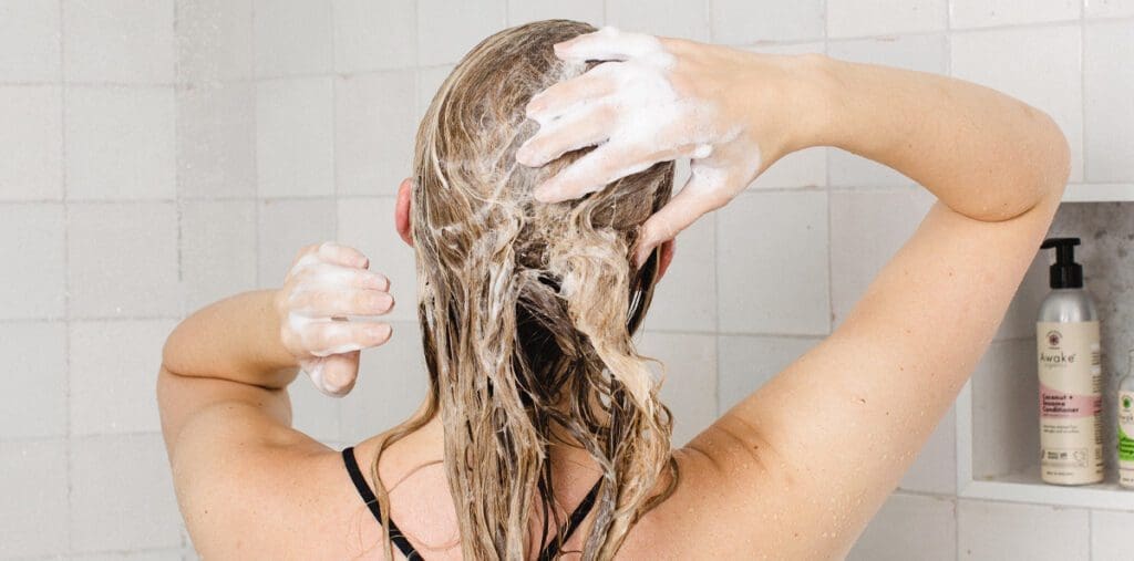 Woman in shower shampooing her hair with natural shampoo.